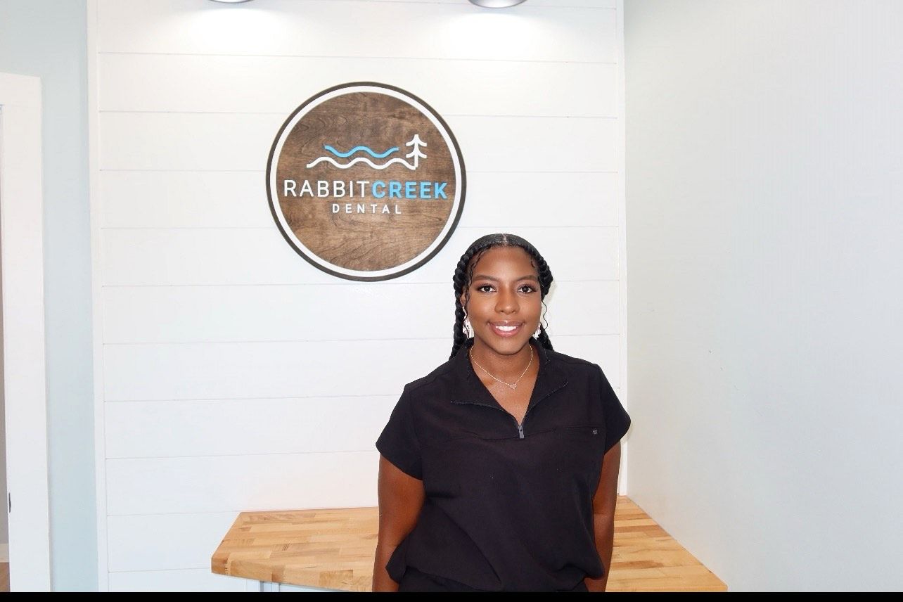 a woman is standing in front of a rabbit creek dental sign .