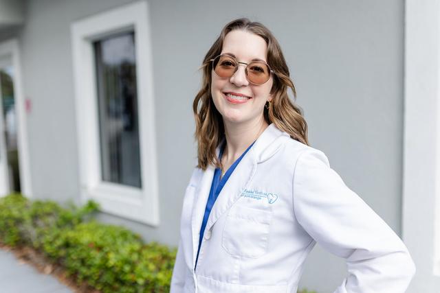 a woman in a lab coat and sunglasses is standing in front of a building .