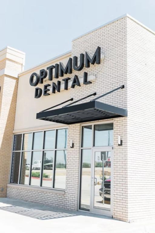 Exterior of the Optimum Dental building with light brick, large windows, and a black awning.