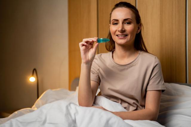 a woman is sitting on a bed holding a mouth guard .