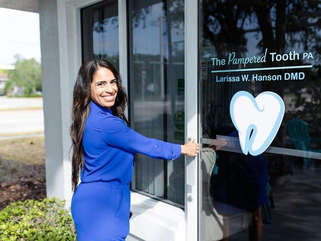 a woman in a blue dress is opening the door of a dental office .