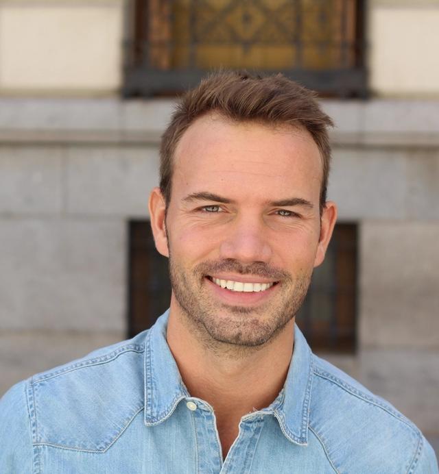 a close up of a smiling man wearing a denim shirt .