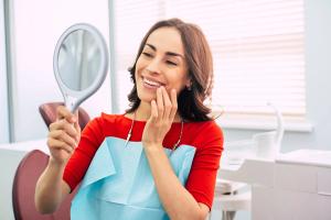 a woman is looking at her teeth in a mirror at the dentist .