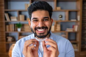 A smiling man holds clear dental aligners.