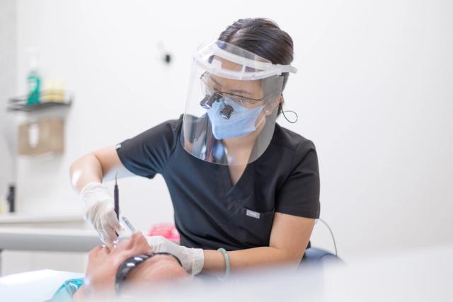 a female dentist wearing a face shield and glasses is working on a patient 's teeth .