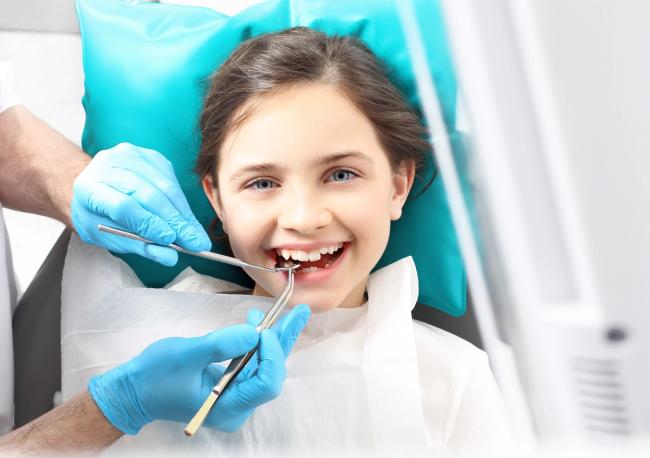 a little girl is having her teeth examined by a dentist .