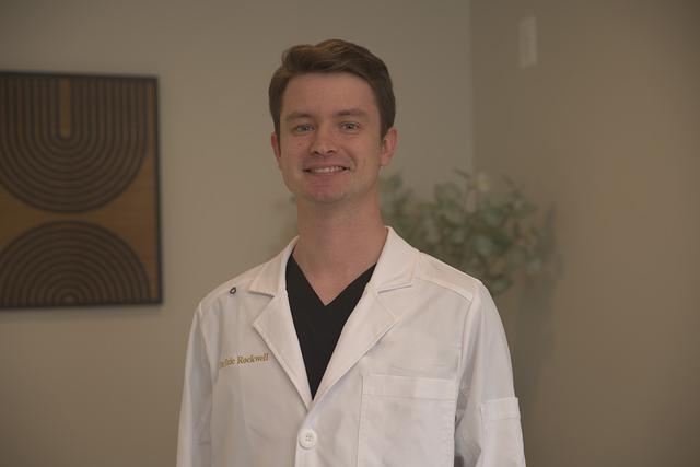 A smiling man in a white lab coat with "Dr. Rockwell" embroidered on it.