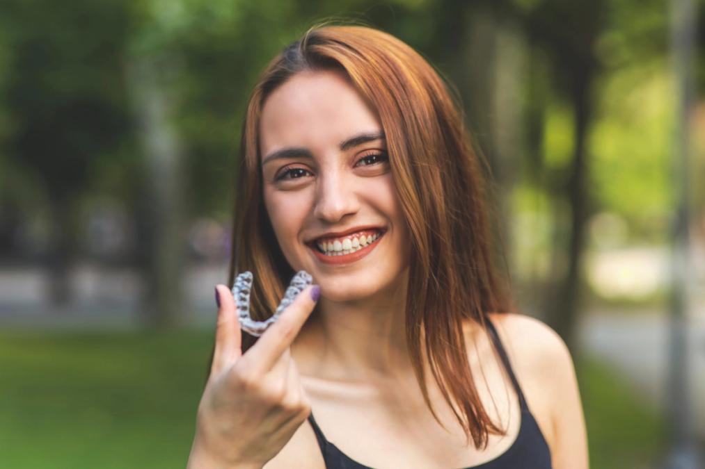 Smiling woman holding a clear dental aligner.
