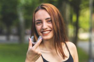 Smiling woman holding a clear dental aligner.