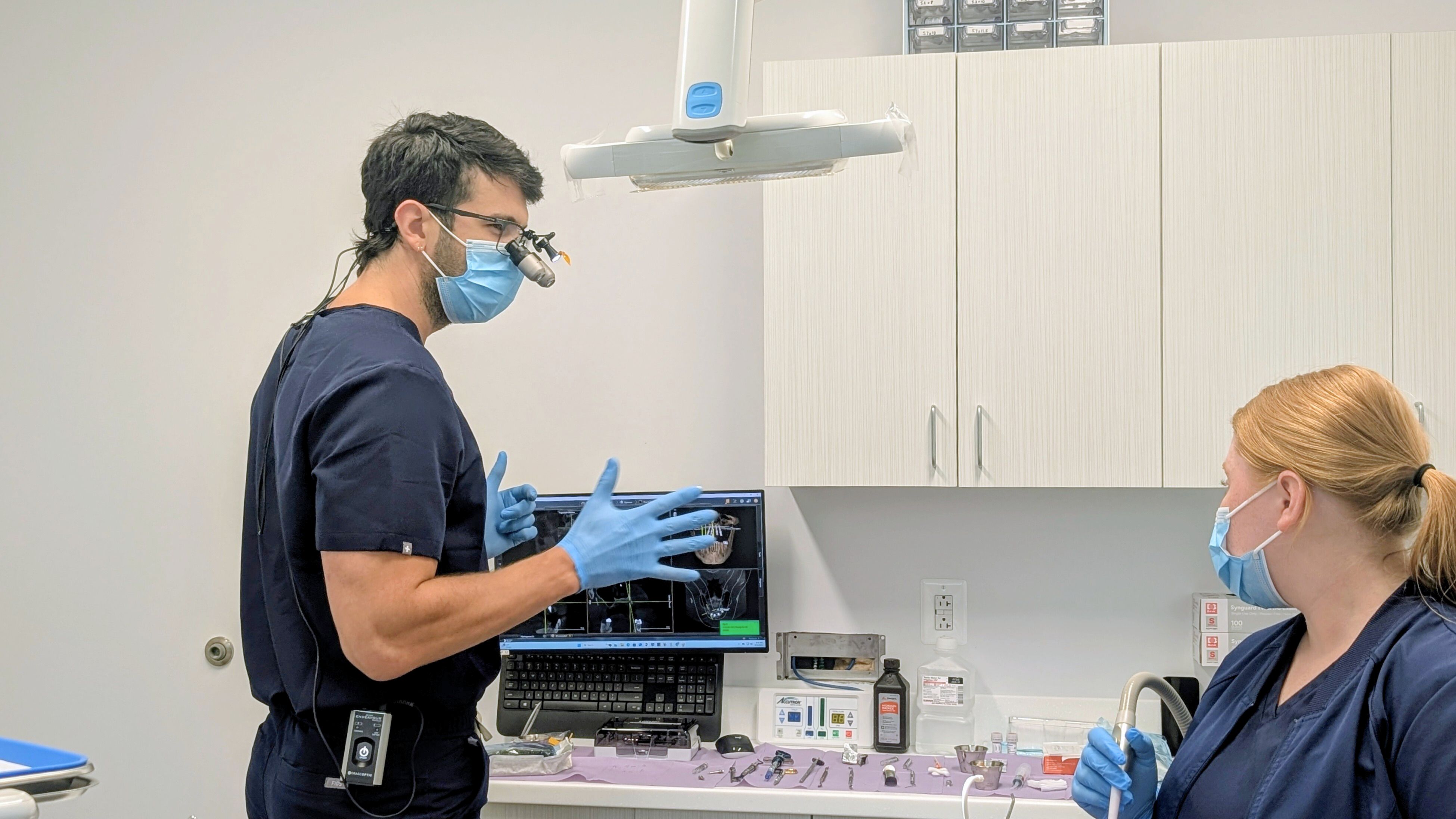 a dentist and a nurse are looking at an x-ray in a dental office .