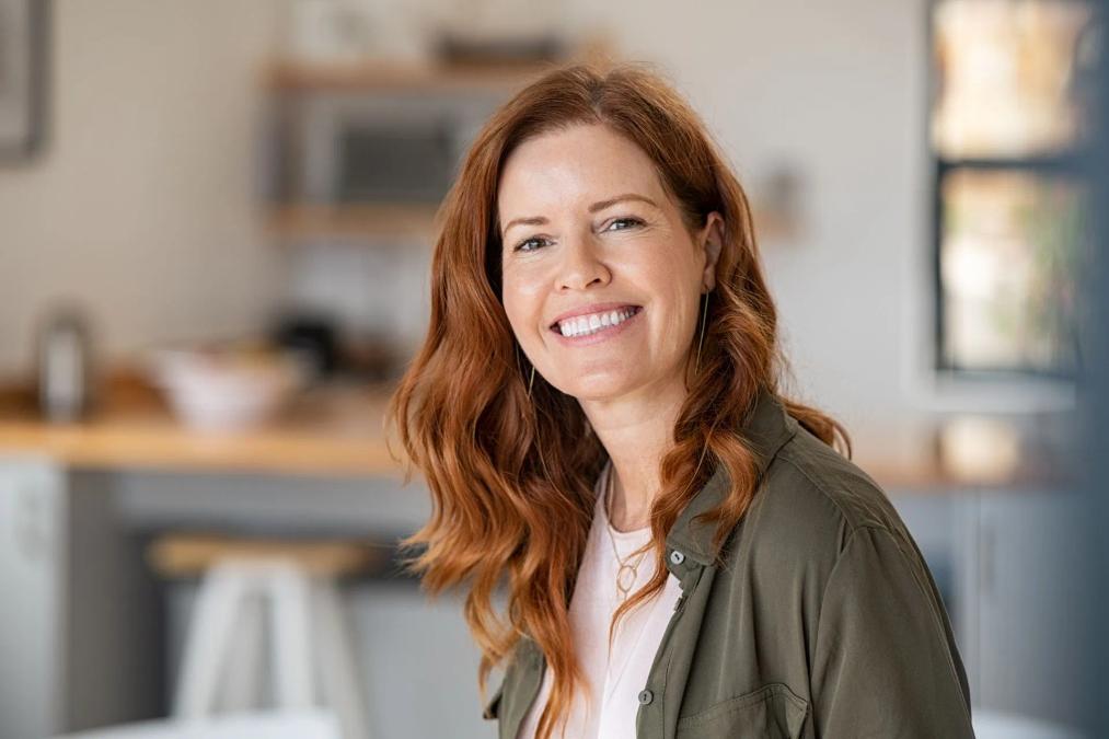 a woman with red hair is smiling for the camera in a kitchen .