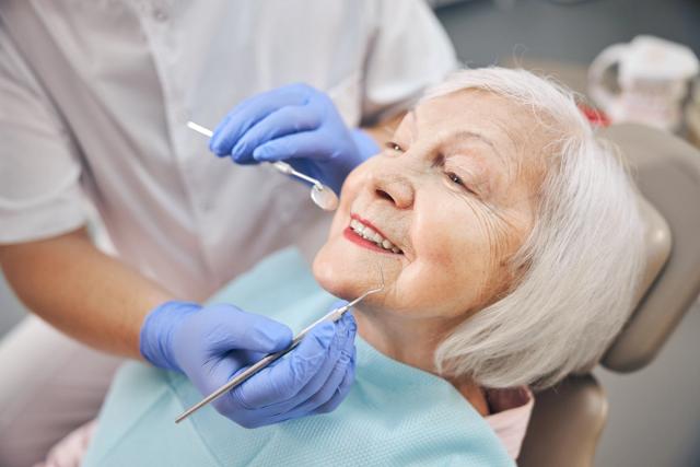 an elderly woman is sitting in a dental chair while a dentist examines her teeth .