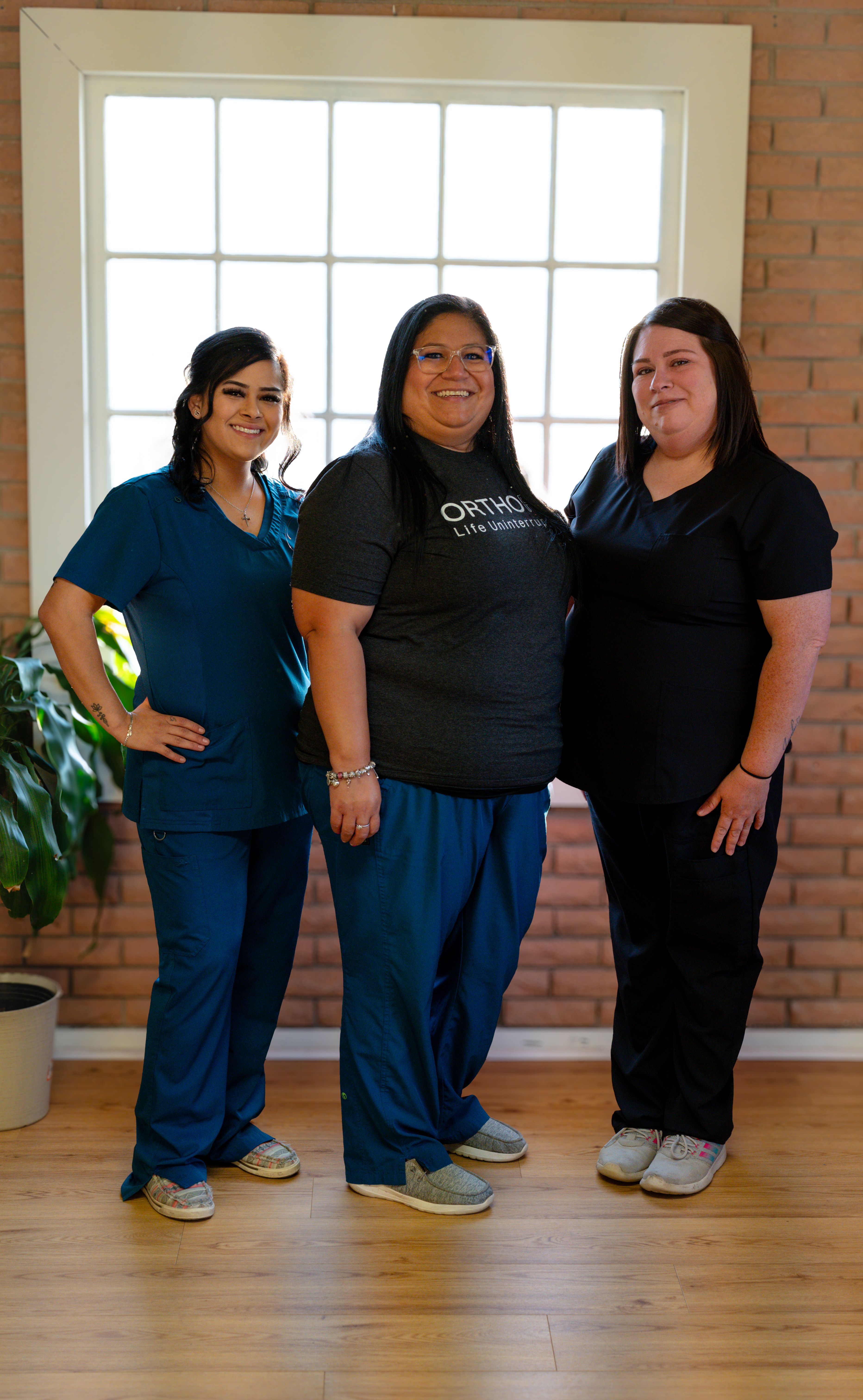 three women are posing for a picture and one has an ortho life shirt on