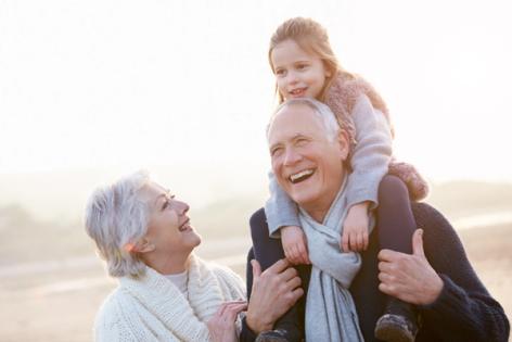 an elderly couple is carrying a little girl on their shoulders on the beach .