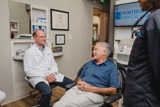 a man is sitting in a dental chair talking to a dentist .