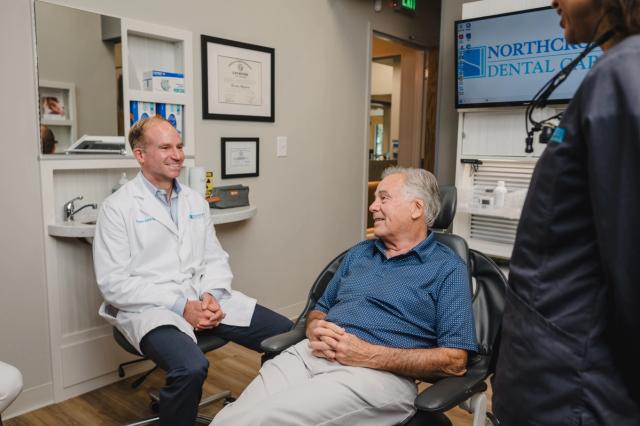 a man is sitting in a dental chair talking to a dentist .