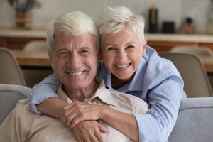 an elderly couple are smiling while sitting on a couch and hugging each other.