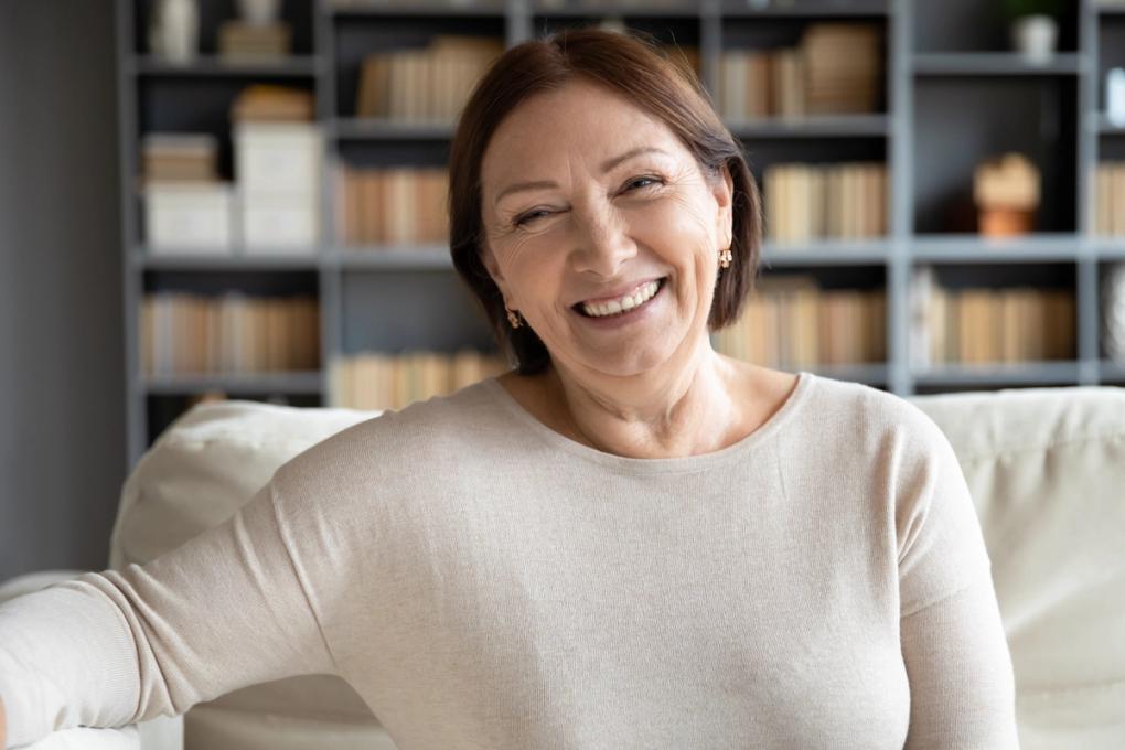 a woman is smiling while sitting on a couch in front of a bookshelf .