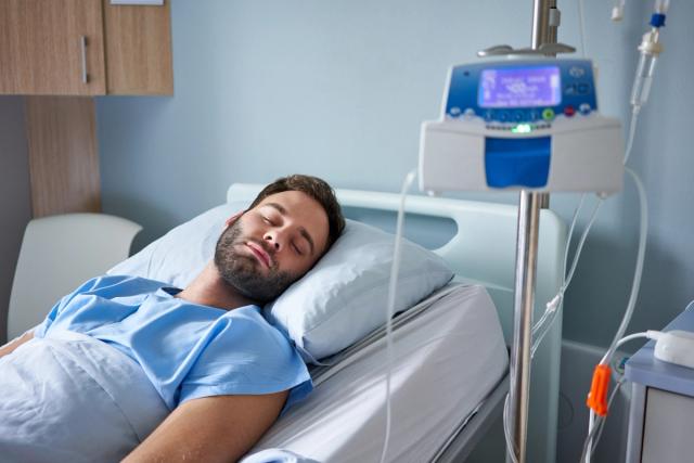 a man is laying in a hospital bed with his eyes closed .