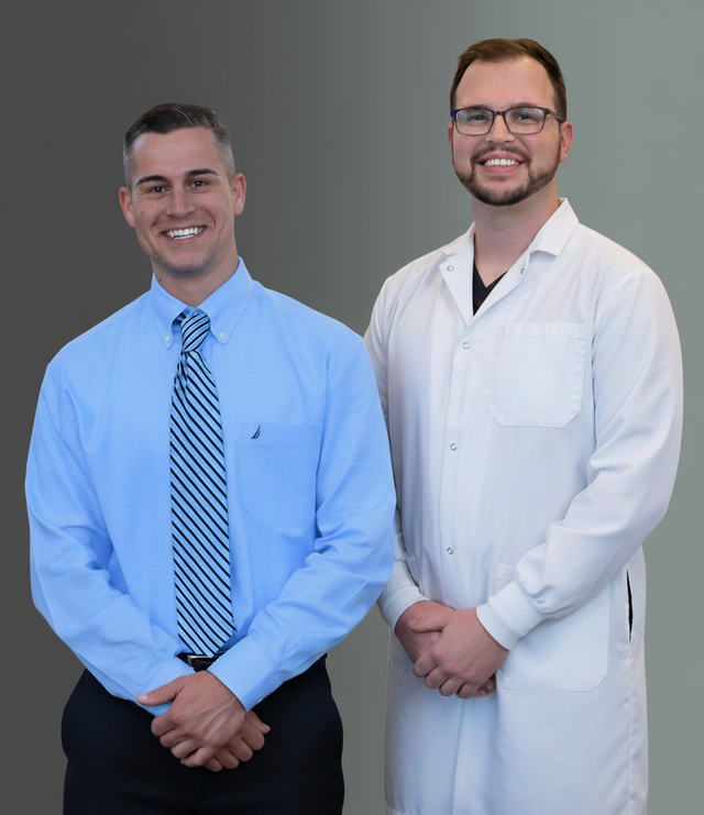 Two smiling men, one in a blue shirt and tie, the other in a white lab coat.