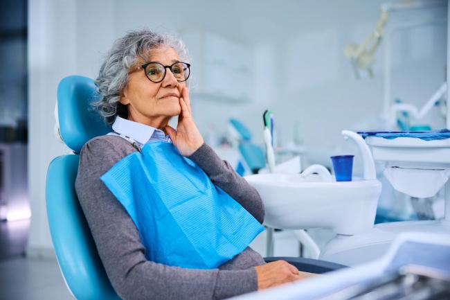 an elderly woman is sitting in a dental chair with her hand on her face .