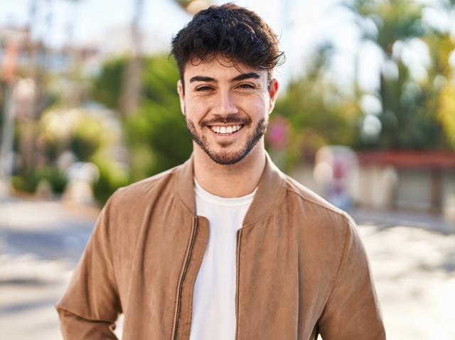 a young man with a beard is smiling for the camera while wearing a brown jacket .