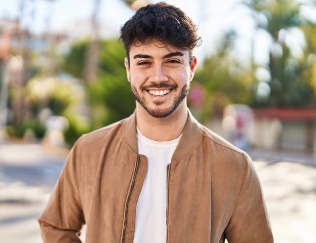 a young man with a beard is smiling for the camera while wearing a brown jacket .