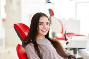 a woman is sitting in a red dental chair and smiling .