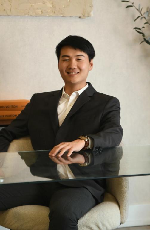 a man in a suit sits at a table with louis vuitton books on the wall behind him