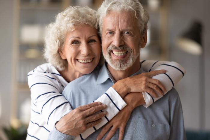 an elderly couple is hugging each other and smiling for the camera .