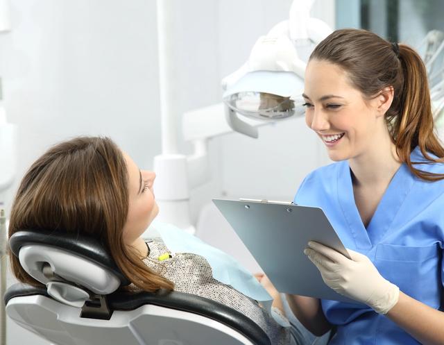 a female dentist is talking to a patient in a dental chair while holding a clipboard .