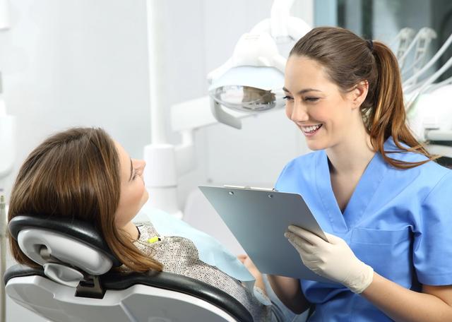 a female dentist is talking to a patient in a dental chair while holding a clipboard .