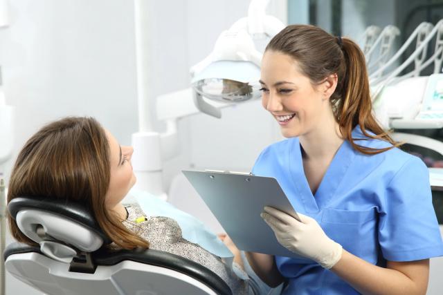 a female dentist is talking to a patient in a dental chair while holding a clipboard .