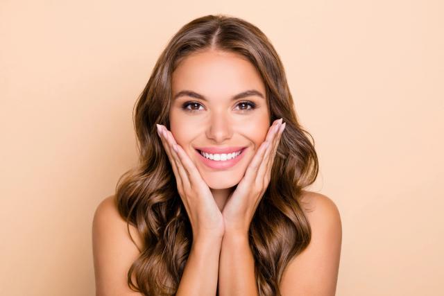 a woman is smiling and touching her face with her hands .