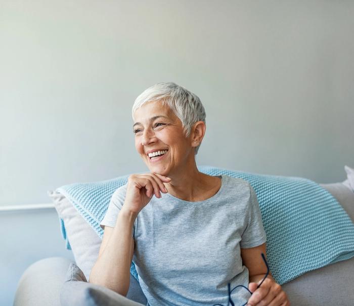 an older woman is sitting on a couch with glasses and smiling .