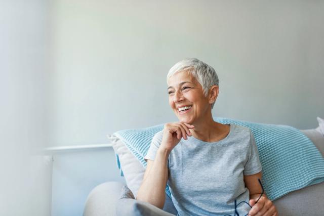 an older woman is sitting on a couch with glasses and smiling .