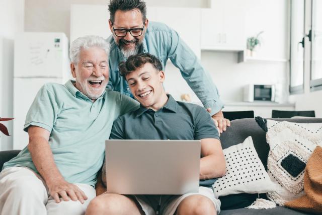 three men are sitting on a couch looking at a laptop computer .