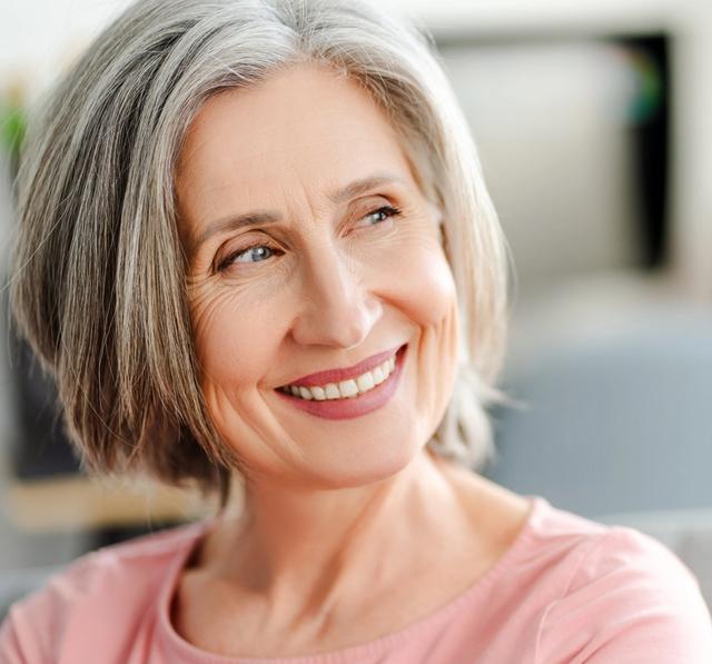 a woman with gray hair is smiling while sitting on a couch .