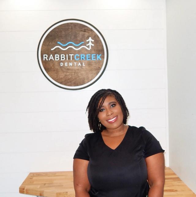 a woman is sitting in front of a rabbit creek dental sign .