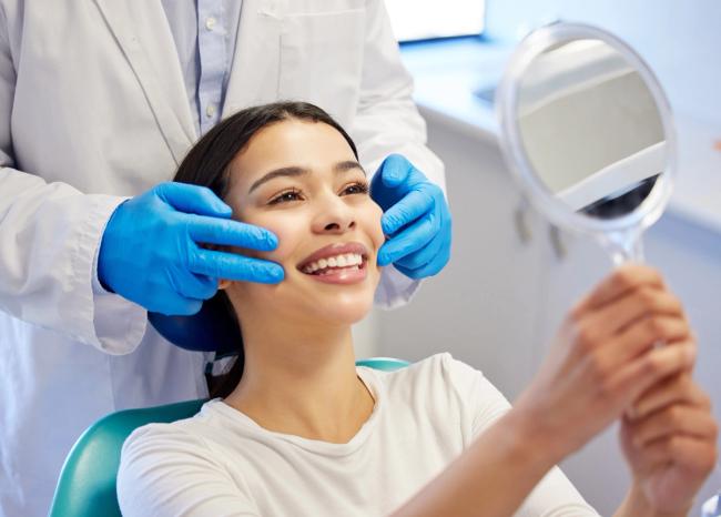 a woman is sitting in a dental chair looking at her teeth in a mirror .