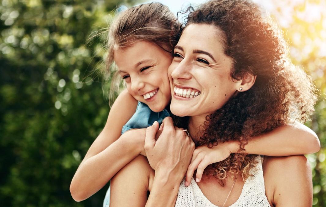 A smiling woman and young girl hugging outdoors.