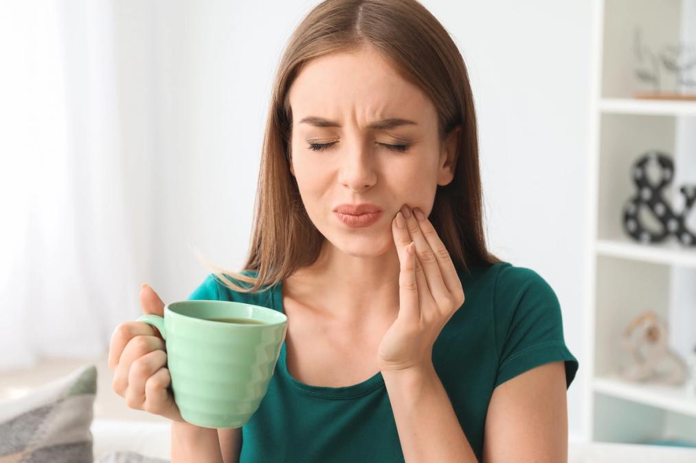 Woman experiencing a toothache while holding a mug.