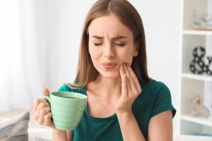 Woman experiencing a toothache while holding a mug.