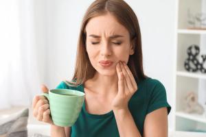 a woman is holding a cup of coffee and having a toothache .