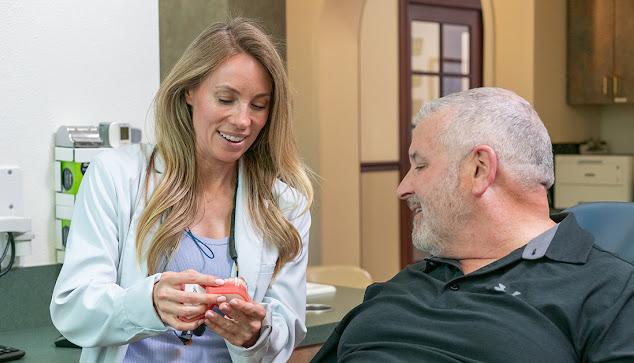 a woman is talking to a man in a dental chair .