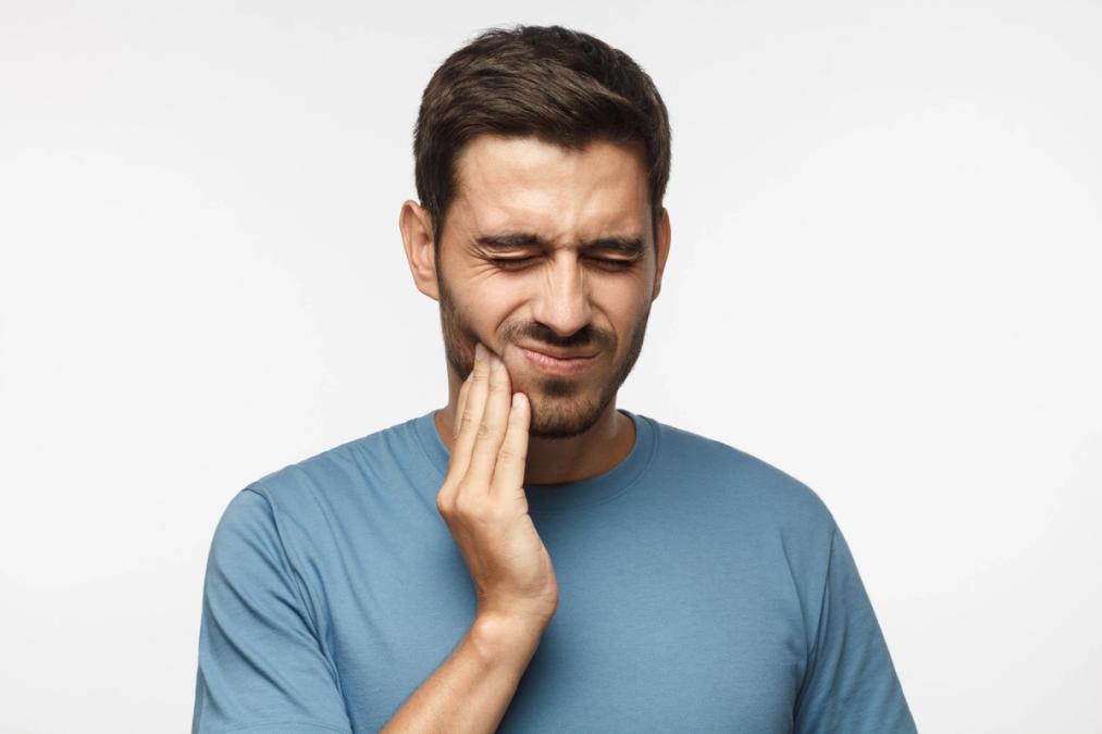 A man with a pained expression clutches his cheek, indicating a toothache.