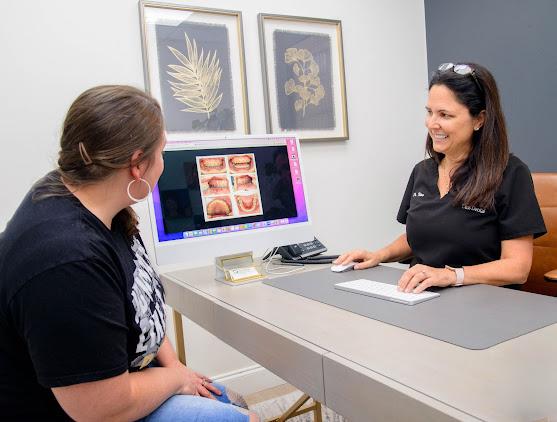 a woman is sitting at a desk talking to a dentist .