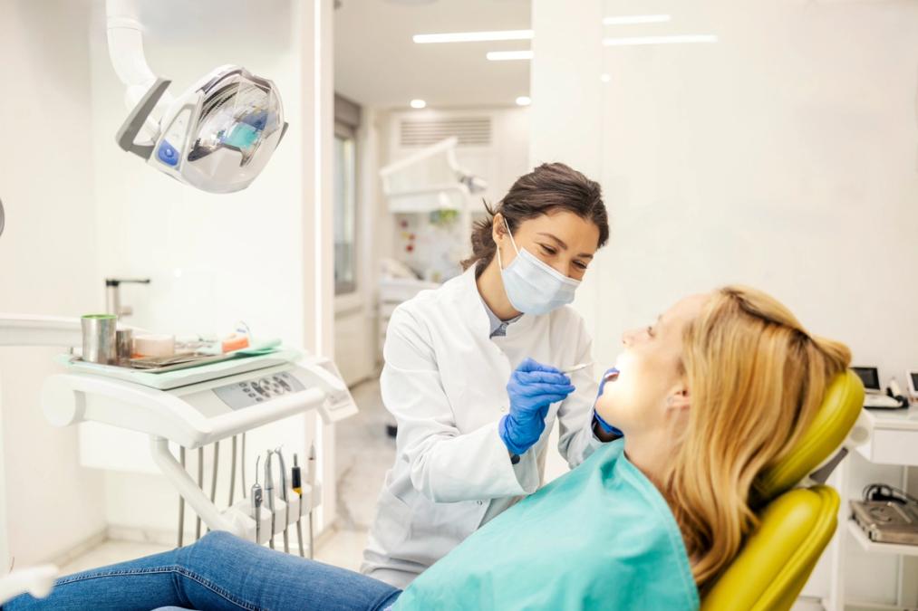 a woman is sitting in a dental chair while a dentist examines her teeth .