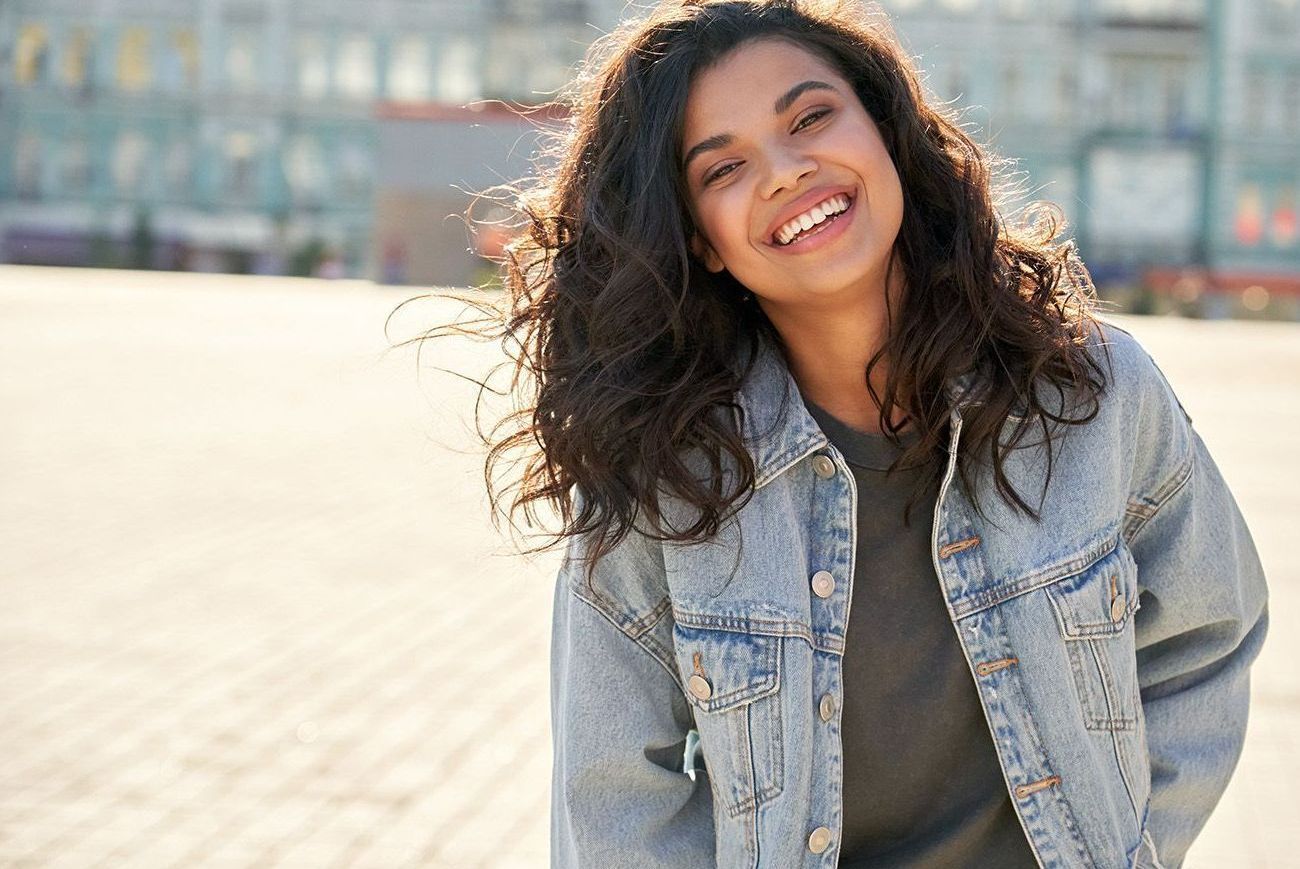 a woman wearing a denim jacket is smiling and looking at the camera .