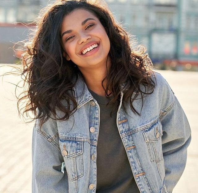 a woman wearing a denim jacket is smiling and looking at the camera .